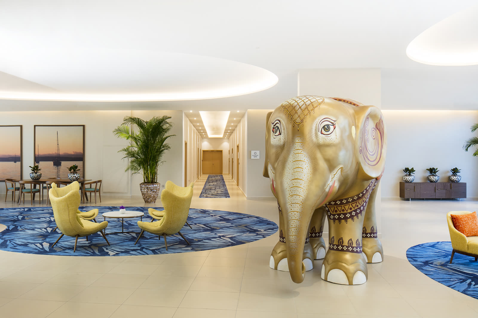 Lobby with a golden elephant sculpture, yellow chairs and a blue patterned rug
