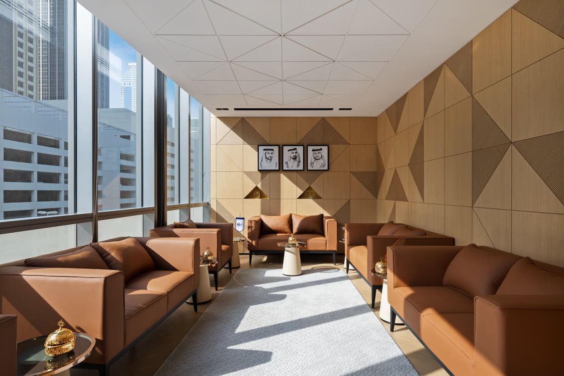 Waiting lounge with tan leather sofas, a faceted timber wall and tall city windows