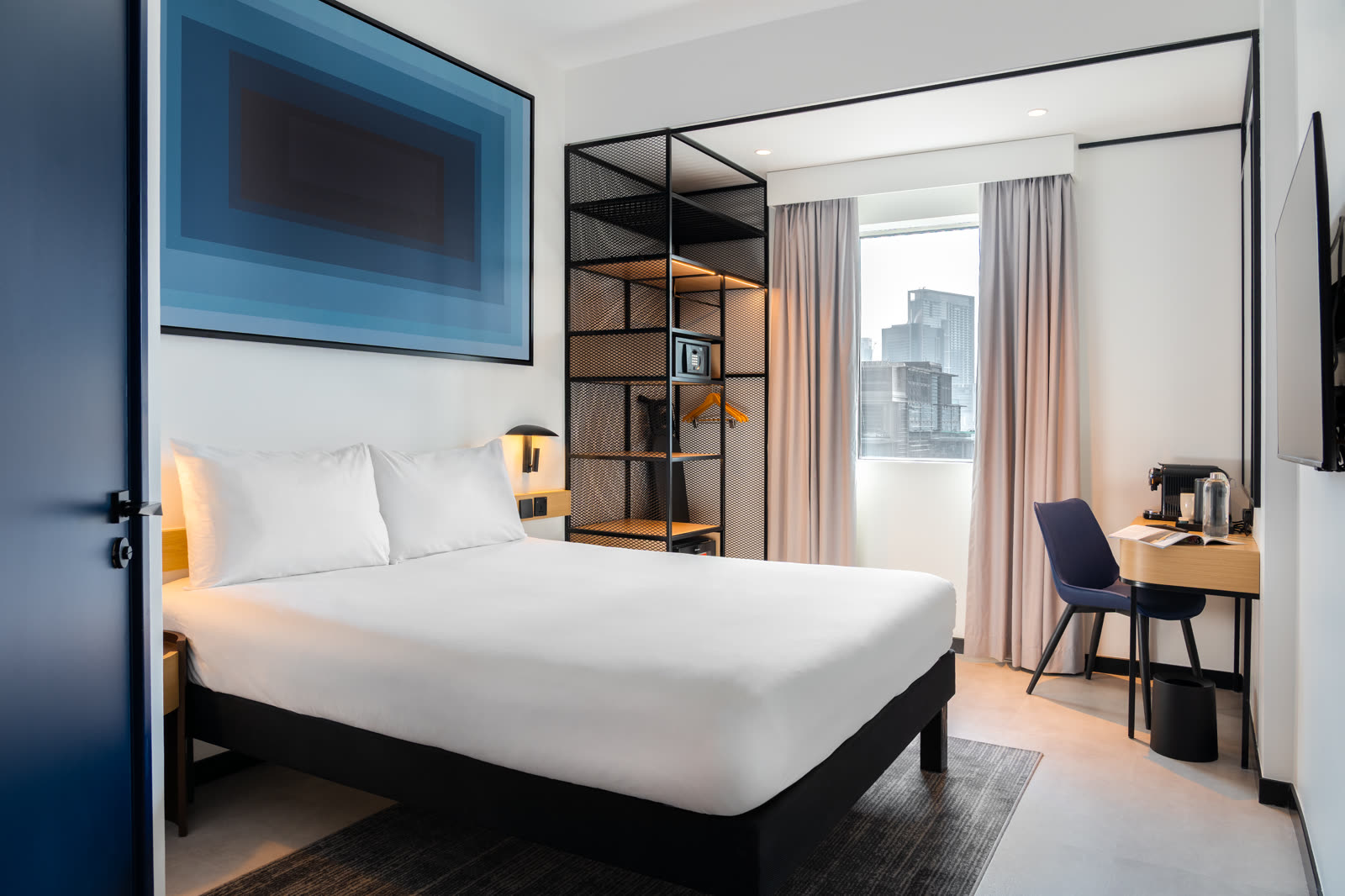 Guest room with a white bed, blue artwork and a black metal wardrobe frame