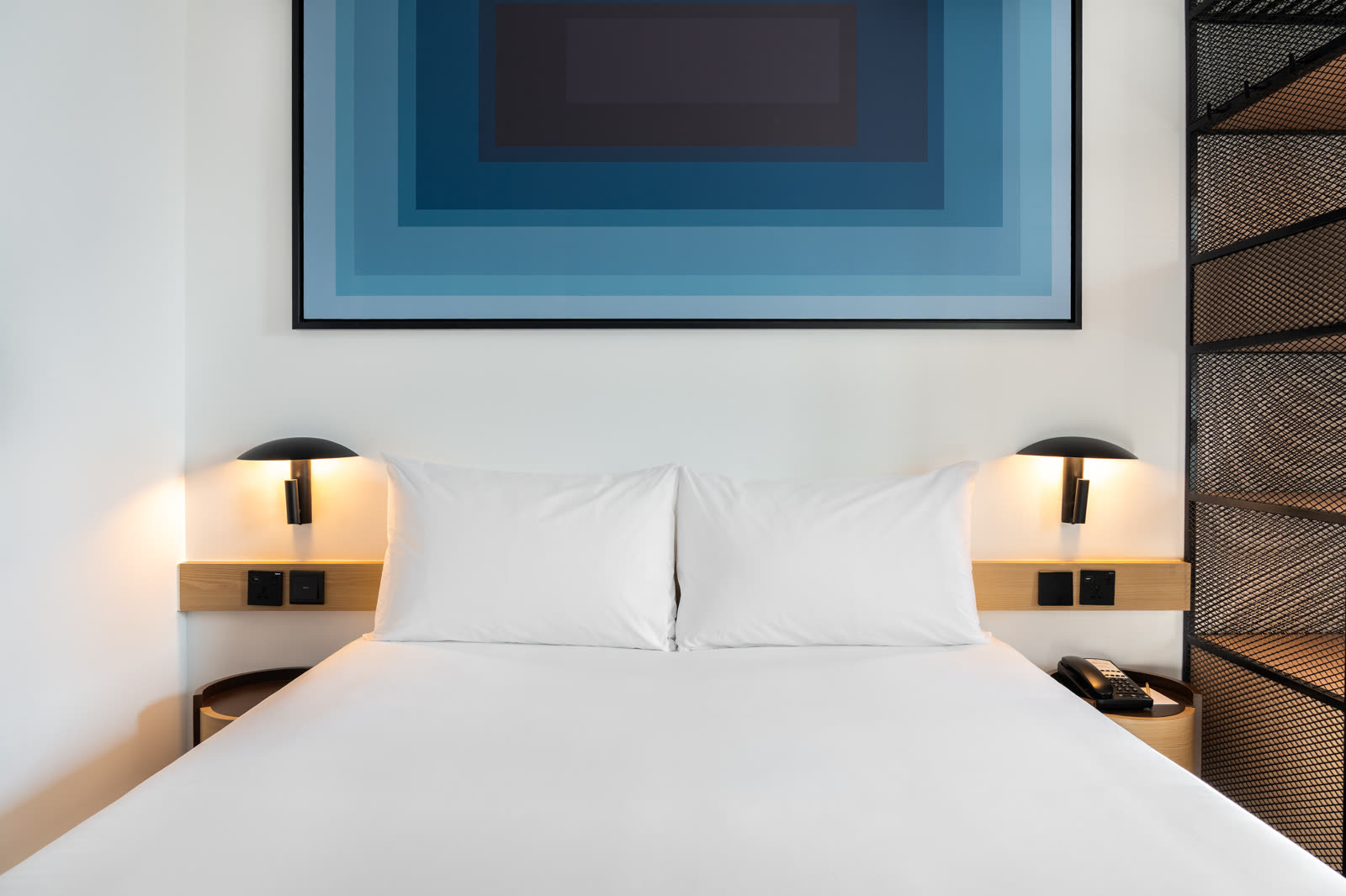 Bed headboard detail under a blue concentric artwork with wall lights