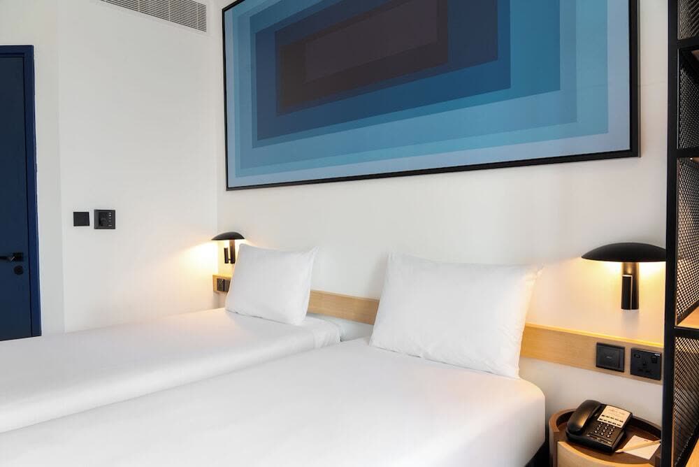 Bed with white linen beneath a blue concentric artwork and wall lights