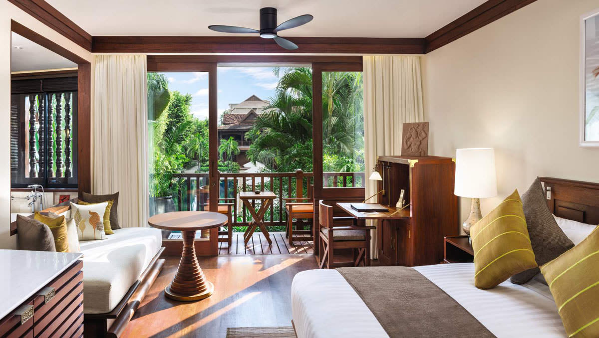 Guest room with a balcony opening onto palm trees and a timber desk