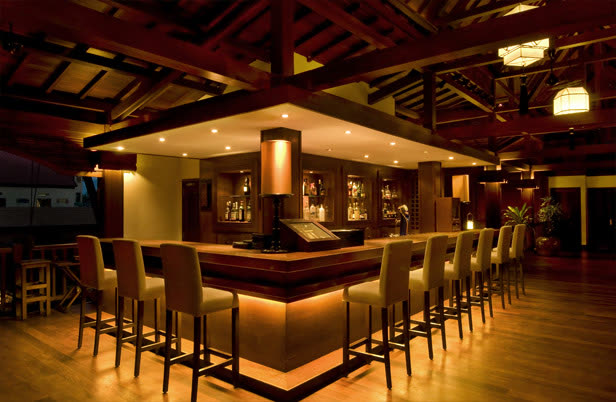 Resort bar with a lit timber counter and high stools under a timber roof