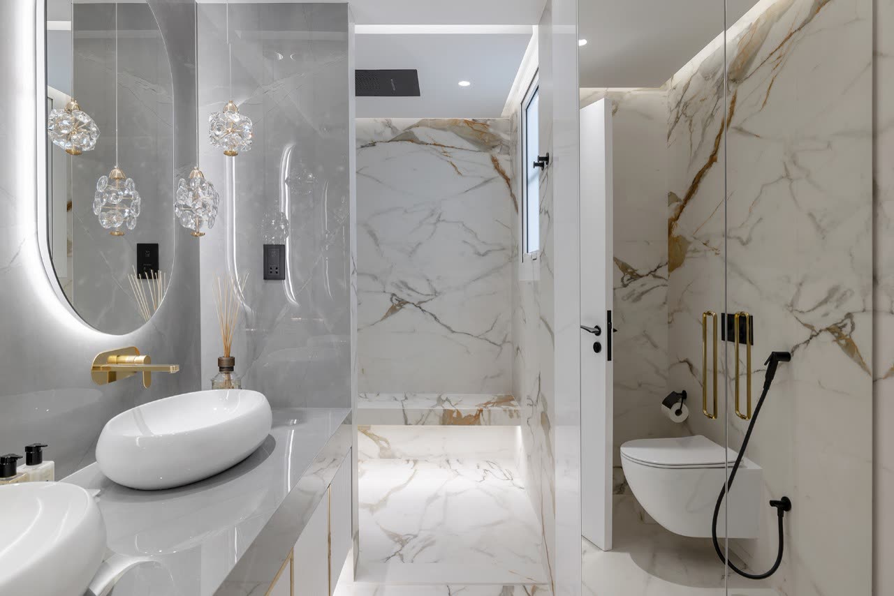 Bathroom with an oval backlit mirror, crystal pendant lights and a marble shower
