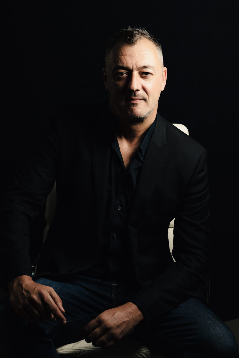 Portrait of Lee Worthington, founder of AndNow, seated in dark clothing against a black background